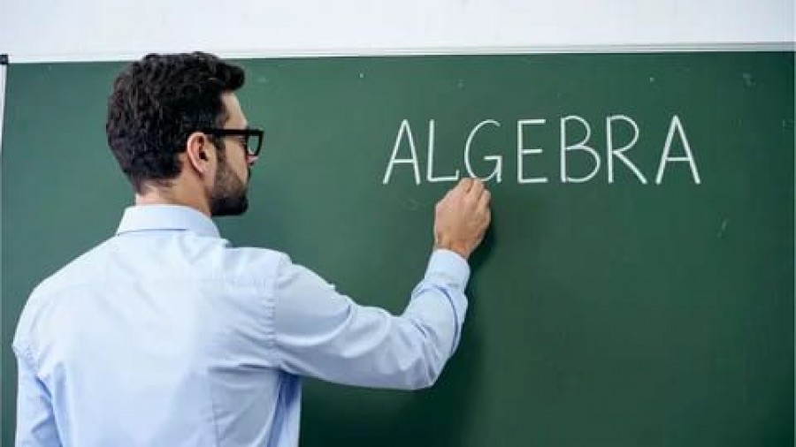 Teacher writing the word algebra on a classroom chalkboard