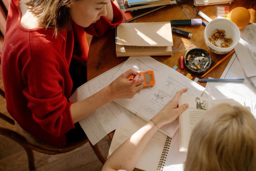 Two students studying math together at a table covered with books and notes.